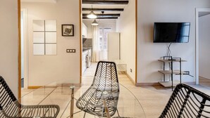 Una sala de estar moderna con televisor, un comedor con sillas y una cocina al fondo.