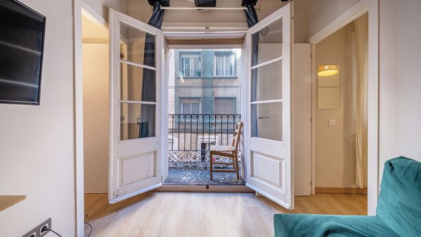 Una habitación con un amplio ventanal que da a un balcón, donde hay una silla y una mesita.