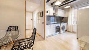 Una cocina moderna con armarios blancos, horno empotrado y lavadora. Cuenta con un comedor con mesa y sillas de vidrio.