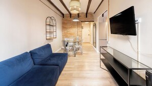 A modern living room with a blue sofa, a glass dining table, and a mounted TV.