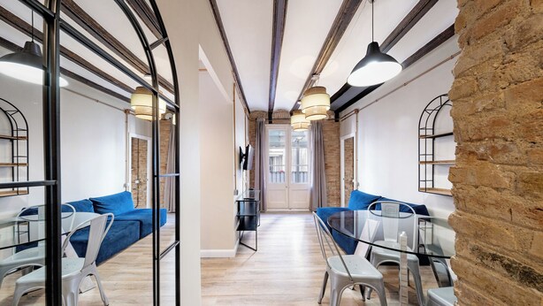 A modern interior with a central corridor, blue sofas, glass tables, and a brick wall.