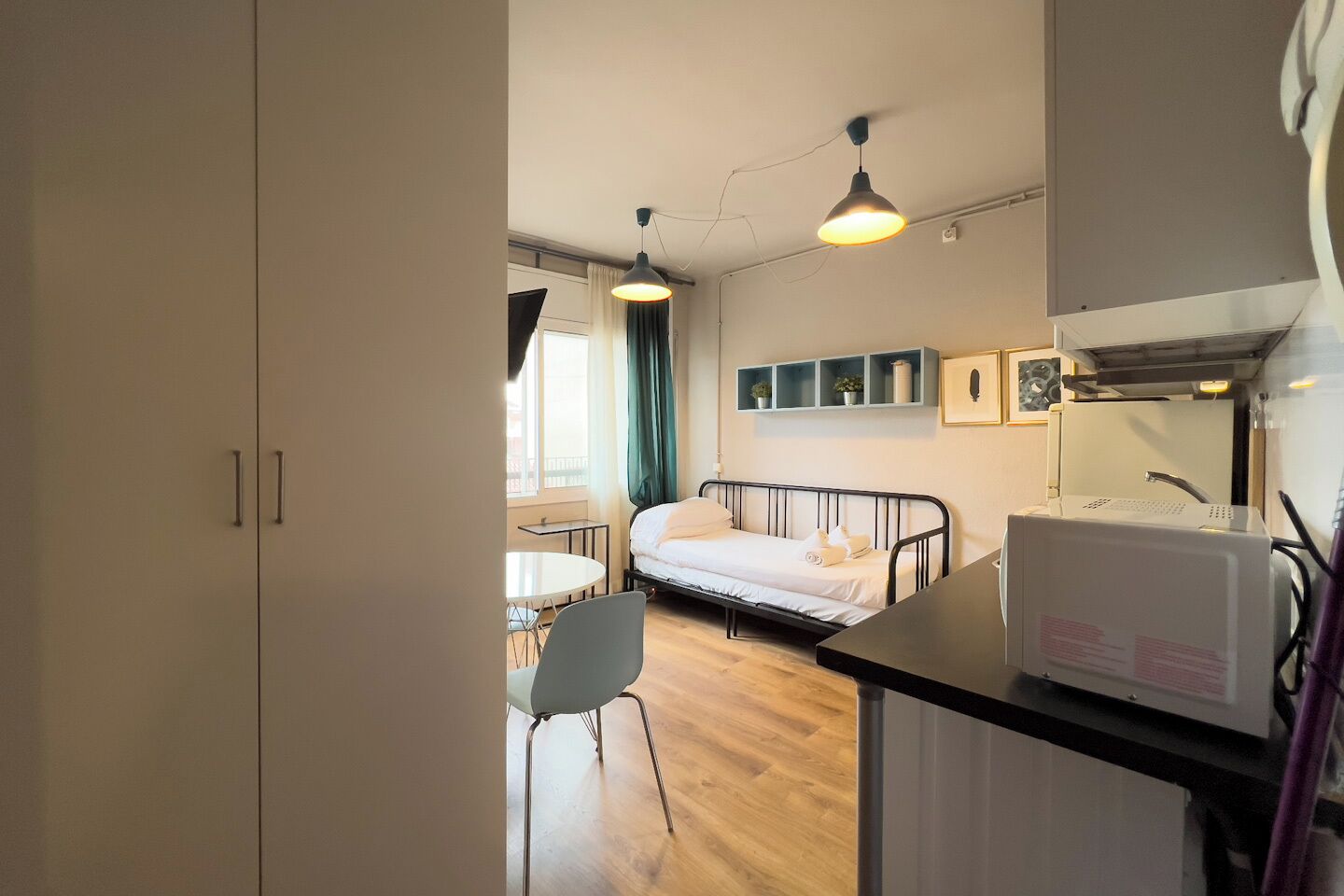 Ein kleines Hotelzimmer mit Bett, Tisch, Stuhl und einer Küchenzeile.