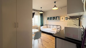 Ett kompakt hotellrum med en säng, ett litet bord, en stol och en liten köksdel.