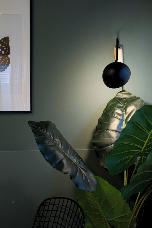 Een kamer met een grote groene plant, een zwarte stoel en een lijst met een afbeelding aan de muur.