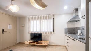 A compact kitchen with a TV on a wooden stand, a window with sheer curtains, and a modern stainless steel range hood. - Bebarceloner Sants Estudios A5 (Barcelona)