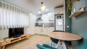 A modern kitchen with a TV on a wooden stand, a dining table with chairs, and a microwave. - Bebarceloner Sants Estudios A5 (Barcelona)