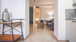A modern living room with a sofa, a coffee table, and a lamp. There is a table with a vase and a chair. The room has a tiled floor and a ceiling light. - Bebarceloner Sants Estudios A6 (Barcelona)