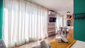 A modern hotel room with a large window, a flat-screen TV, a dining area with a table and chairs, and a kitchen area with a microwave and a coffee machine. - Jaume Atico 509 - Studio Apartment, Sleeps 2 (Barcelona)