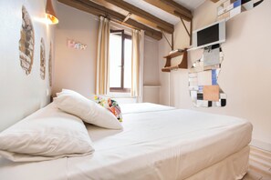 A bed with white bedding, a colorful pillow, a window with curtains, a mounted TV, and a wall with a 'HAPPY' sign.