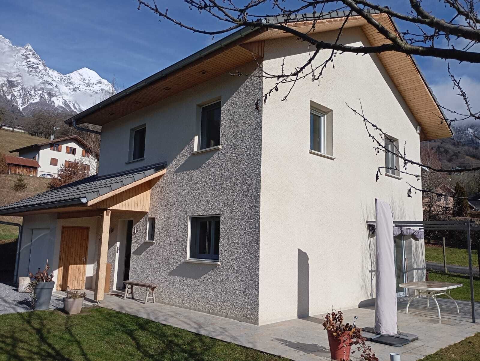 Une maison à deux étages avec une façade en pierre, un toit en bois et un petit porche doté d’un banc.