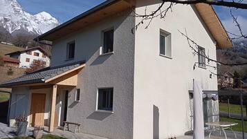 Une maison à deux étages avec une façade en pierre, un toit en bois et un petit porche doté d’un banc.
