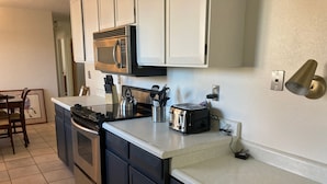 A compact kitchen with a microwave, toaster, kettle, and a small dining area with a chair and table. - Charming, vintage 3-bedroom house in Arvada with AC (Arvada)