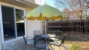 An outdoor patio with a table and chairs, a yellow umbrella, and a wooden fence in the background. - Charming, vintage 3-bedroom house in Arvada with AC (Arvada)