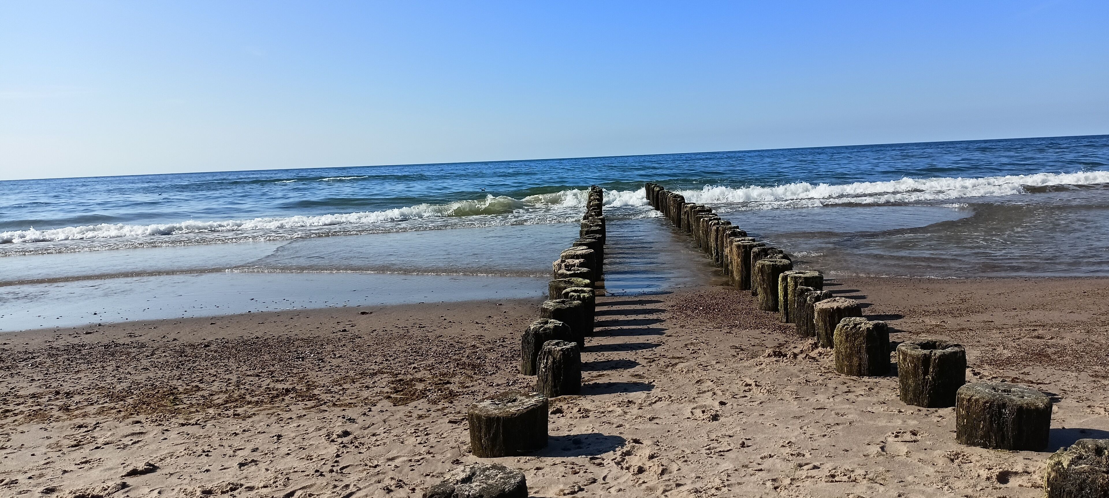 A beach with a wooden jetty extending into the ocean.
