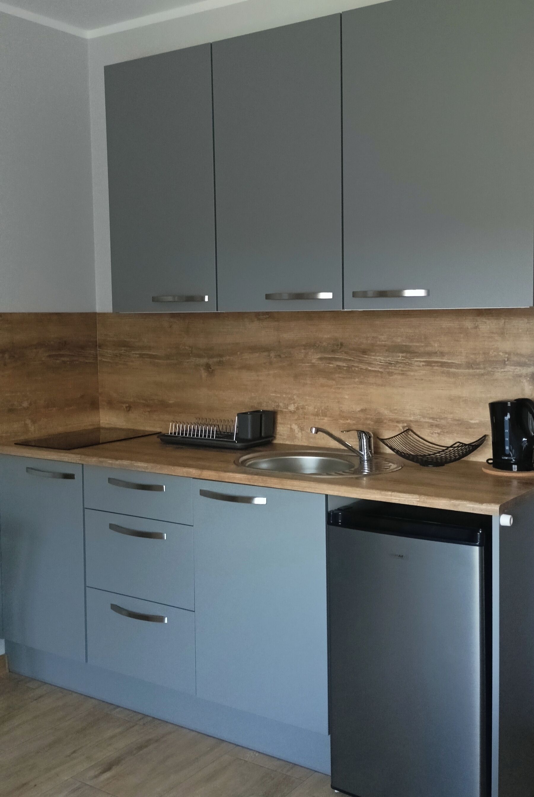 A modern kitchen with grey cabinets, a wooden countertop, a sink, a kettle, and a dishwasher.