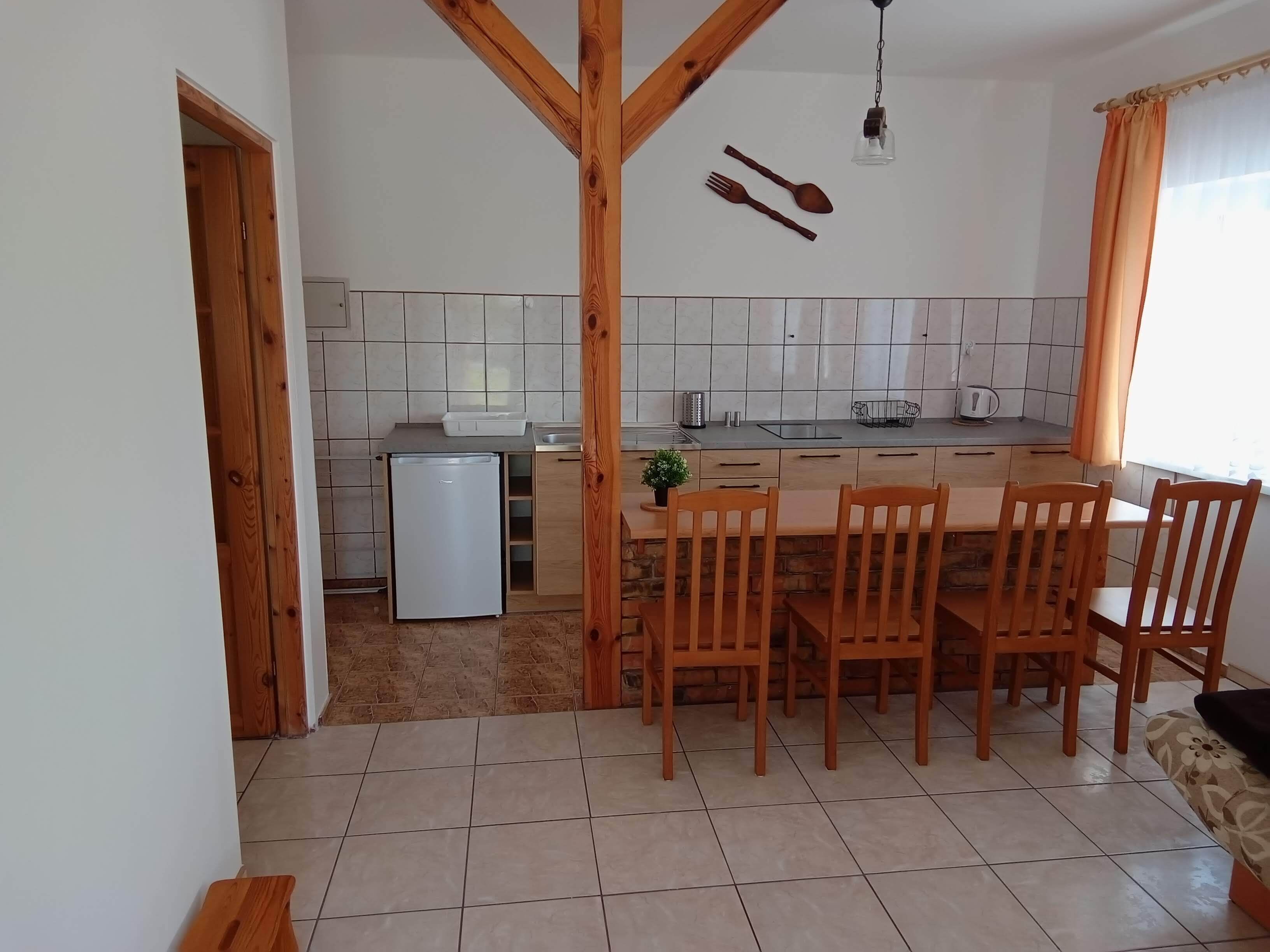 A kitchen with a dining area, wooden beams, a refrigerator, and a small potted plant.