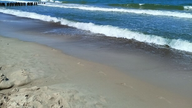 Een strand met blauwe lucht, golven en een houten steiger.