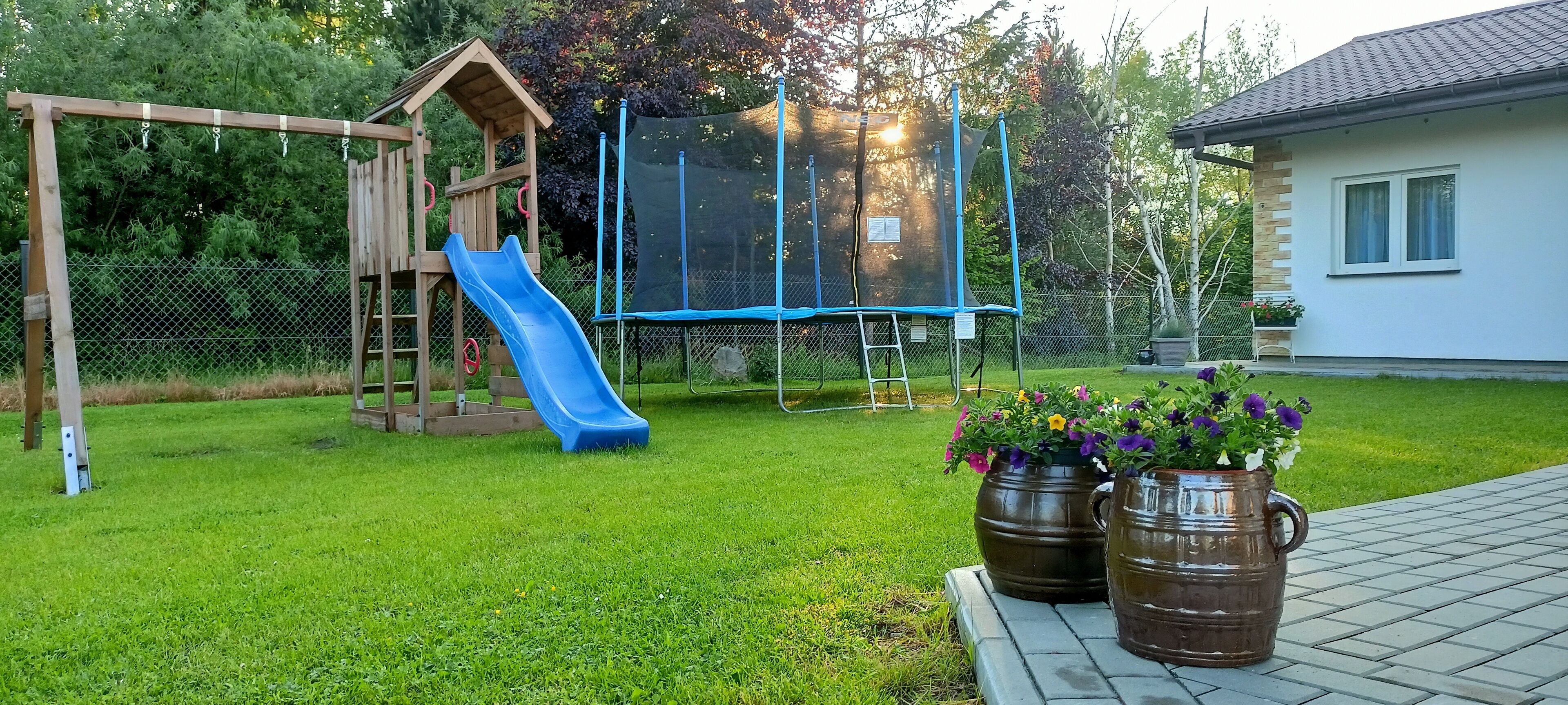 A backyard with a wooden play structure, a trampoline, and a house.