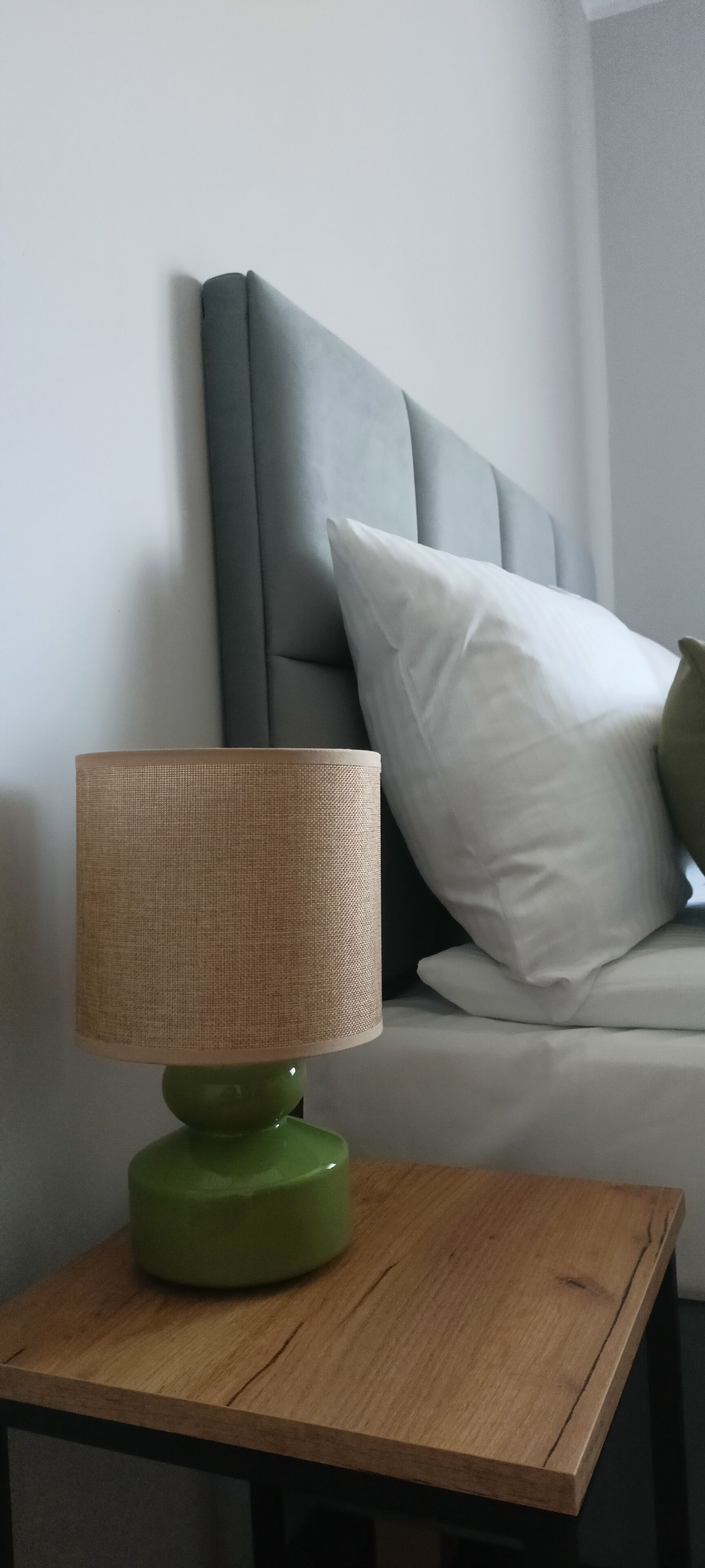A green table lamp with a woven shade on a wooden nightstand.
