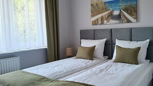 Een net opgemaakt bed met witte lakens en twee kussens, een hoofdbord en een schilderij van een strand.