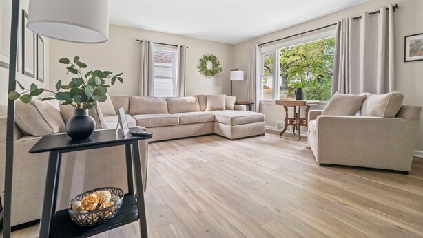 A modern living room with a sectional sofa, a small side table, and a large window with curtains. - Copper Hill Home in Walnut Creek (Sugarcreek)