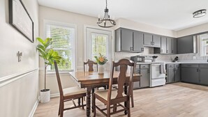 A dining area with a wooden table and chairs, a chandelier, and a view of the kitchen with grey cabinets. - Copper Hill Home in Walnut Creek (Sugarcreek)