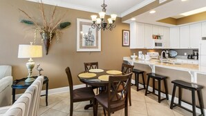 Une cuisine moderne avec des meubles blancs, un îlot central doté de tabourets et un coin repas avec une table ronde et des chaises.