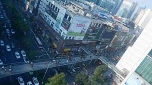 Eine belebte Stadtstraße mit einer Fußgängerbrücke und hohen Gebäuden.