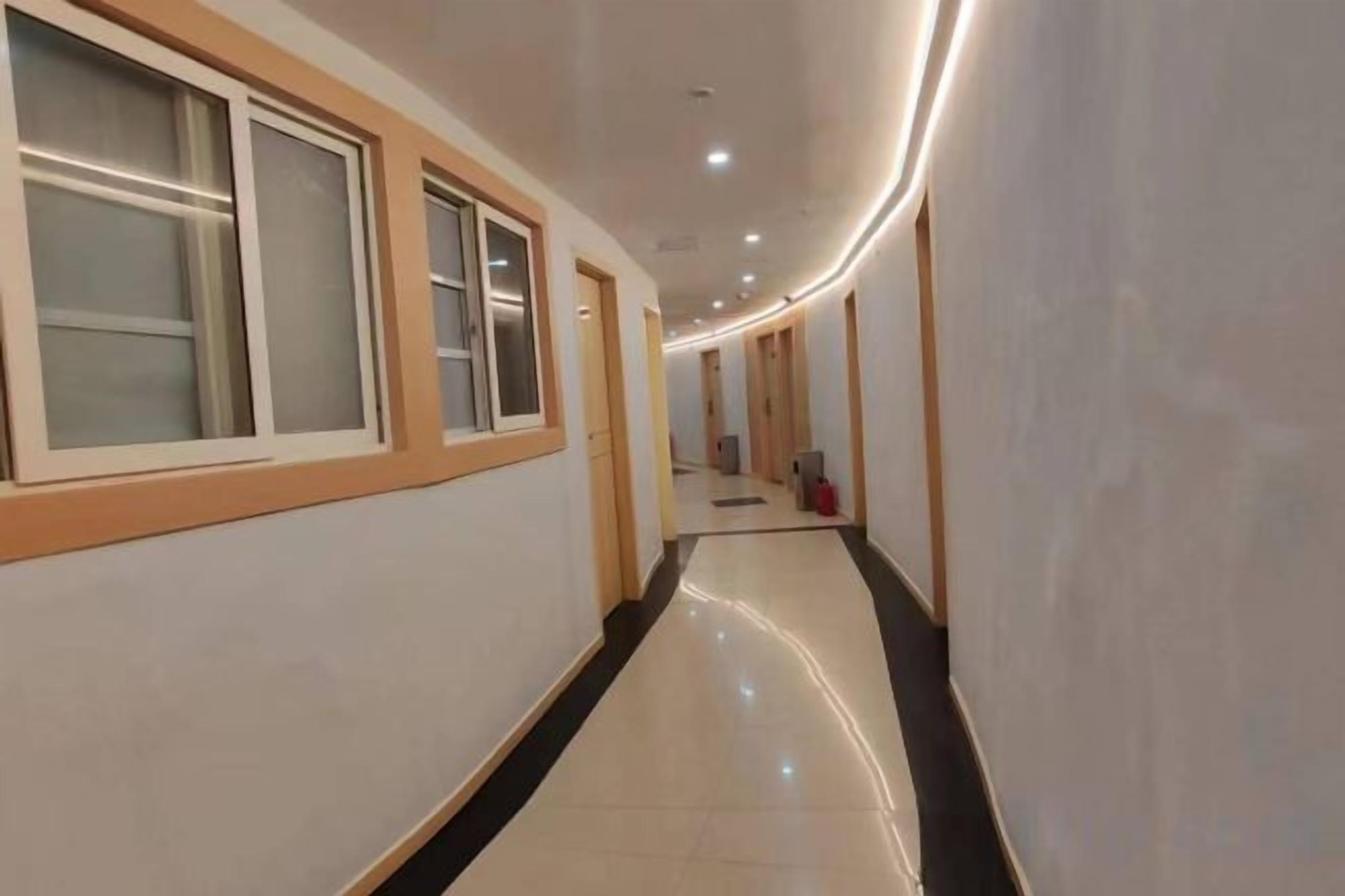 A hotel corridor with a polished floor, doors on the left, and a red object in the distance.