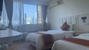 Ein Hotelzimmer mit zwei Betten, einem Schreibtisch und einem großen Fenster mit Vorhängen.