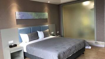 A modern bedroom with a large bed, a nightstand, a wall-mounted artwork, and a frosted glass window.