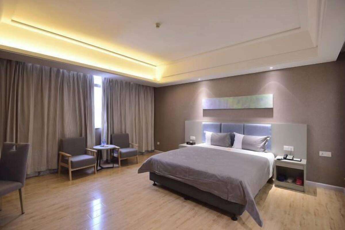 Una habitación de hotel moderna con una cama grande, dos sillones, una mesita y una mesita de noche.
