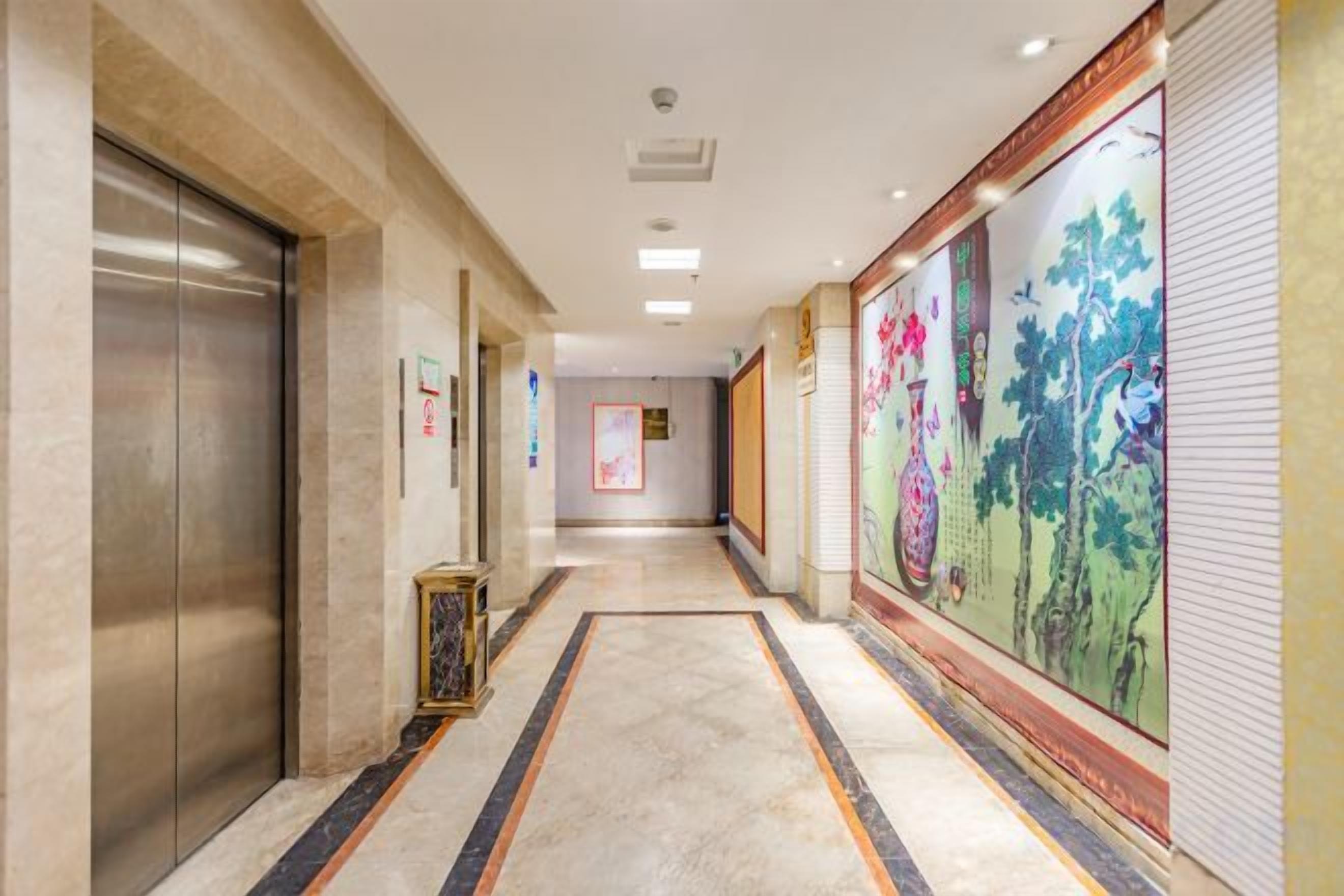 A hotel corridor with an elevator, a patterned carpet, and a mural on the wall.