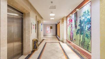 A hotel corridor with an elevator, a patterned carpet, and a mural on the wall.