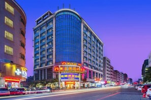 A hotel with a curved facade, multiple floors, and illuminated signage. - M Hotel (Dongguan Haichao) (Dongguan)
