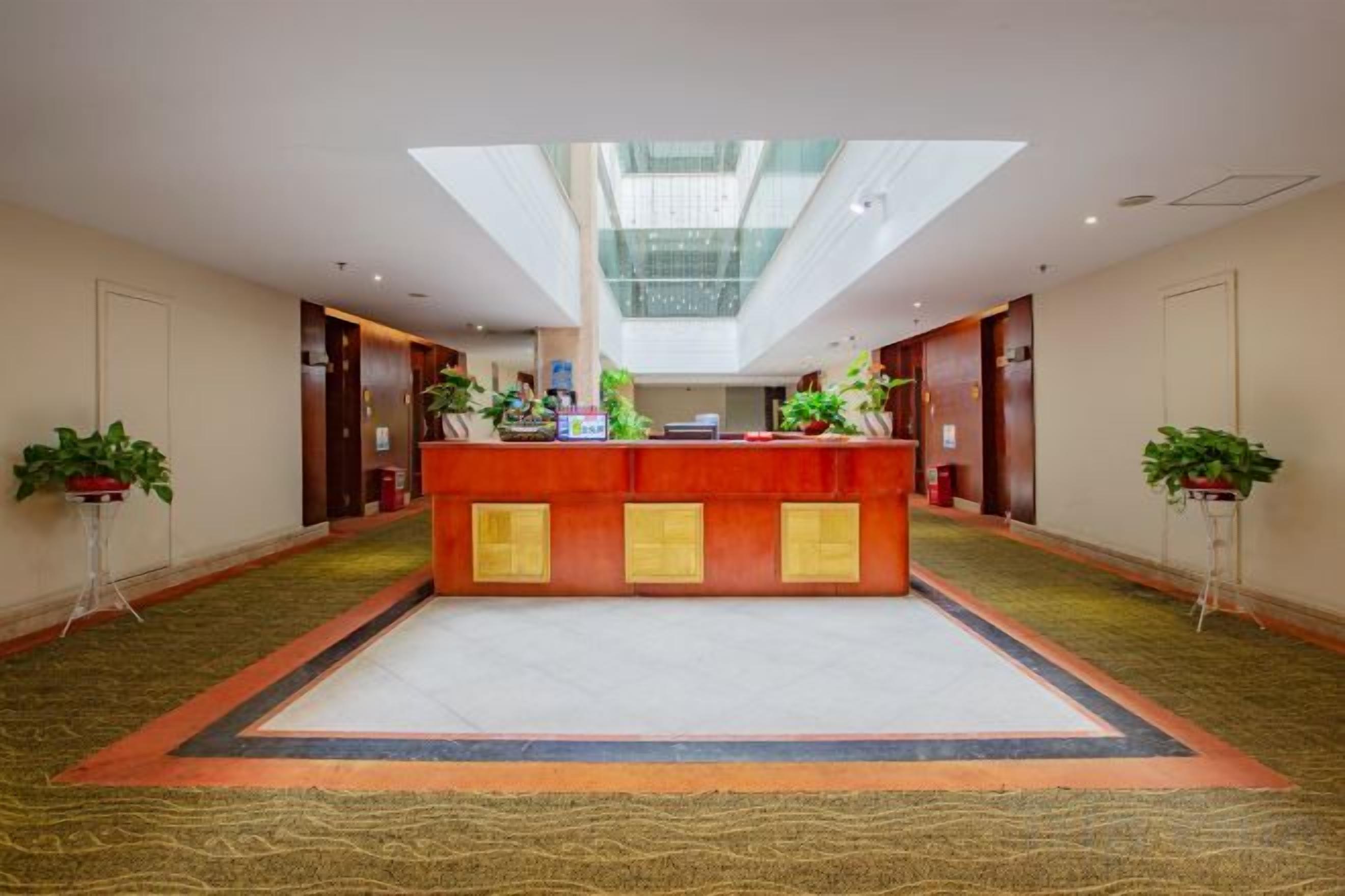 A hotel lobby with a reception desk, potted plants, and a high ceiling with skylights.