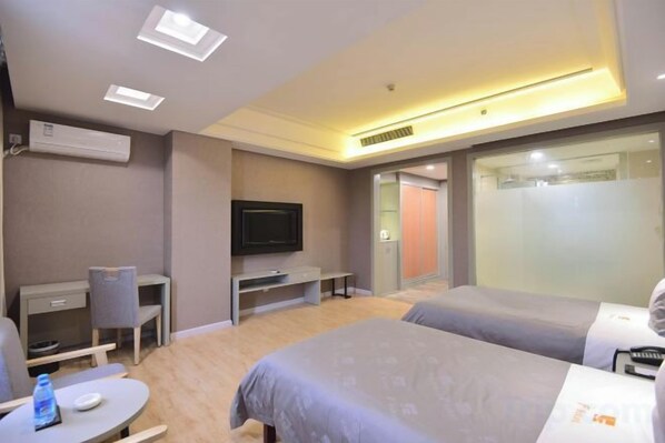 Habitación de hotel con cama, escritorio, silla, televisor y baño visible a través de una puerta de cristal.