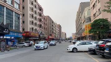 A street lined with multi-story buildings, parked cars, and various storefronts.