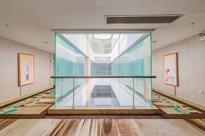 Un pasillo de hotel con un ascensor de cristal, alfombra estampada y cuadros en las paredes.