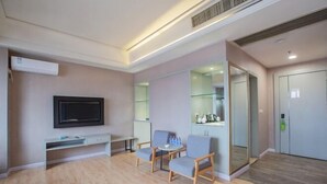 A modern hotel room with a flat-screen TV, a small table, two armchairs, and a glass partition wall. - M Hotel (Dongguan Haichao) (Dongguan)