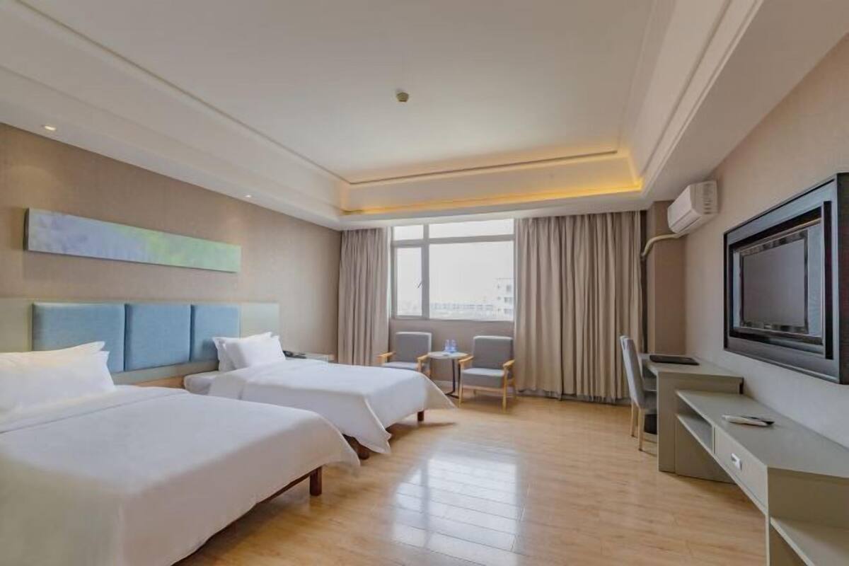 Habitación de hotel con dos camas, televisor, escritorio y ventana con cortinas.