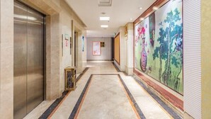 A hotel corridor with a marble floor, a large mural on the right wall, and an elevator on the left. - M Hotel (Dongguan Haichao) (Dongguan)