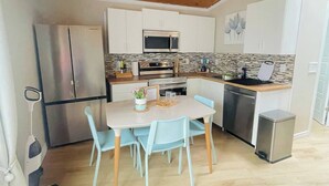 A compact kitchen with wooden ceiling, white cabinets, stainless steel appliances, and a dining area with light blue chairs. - private suite (the skylight) (Lower Sackville)