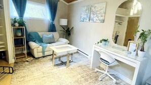 A cozy room with a wooden ceiling, a white desk with a chair, a sofa with blue cushions, and a small plant on the desk. - private suite (the skylight) (Lower Sackville)
