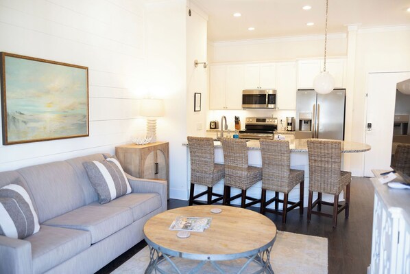 A modern kitchen with white cabinets, stainless steel appliances, and a dining area with wicker chairs.