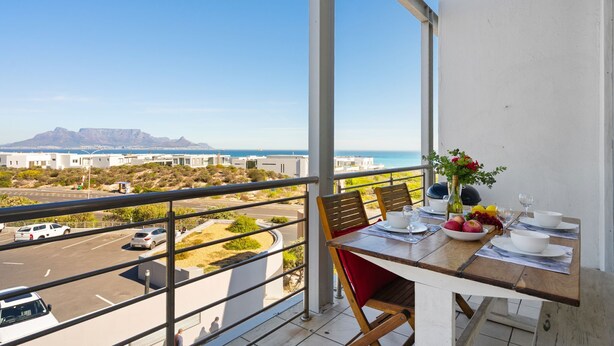 Un balcon avec une table dressée pour le dîner, offrant une vue sur un parking et un paysage montagneux.