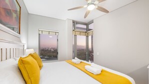 Une chambre d’hôtel avec un grand lit, un ventilateur de plafond et une vue sur la ville par les fenêtres.