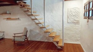 Eine Treppe mit Holzstufen und ein Stuhl in einem Raum mit Holzdielen und weißen Wänden.
