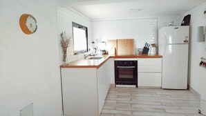 Eine kompakte Küche mit weißen Schränken, einer Holzarbeitsplatte, einem Einbauofen und einem Kühlschrank.