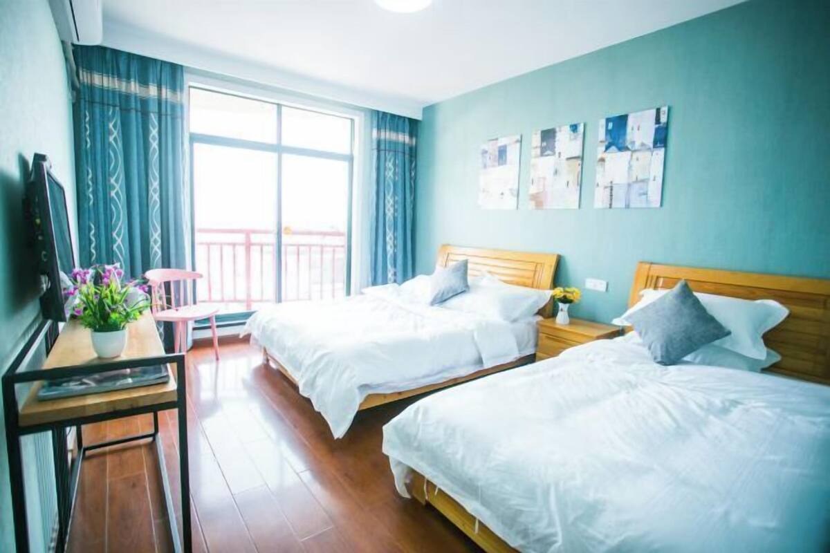 Habitación de hotel con dos camas, un escritorio, una silla y un balcón con cortinas.